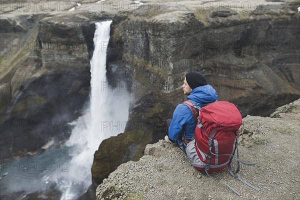 Hiker with backpack on cliff by Haifoss waterfall in Iceland