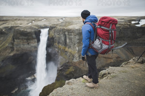 Hiker with backpack on cliff by Haifoss waterfall in Iceland