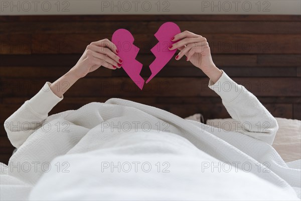 Woman holding aloft pink broken heart while lying in bed