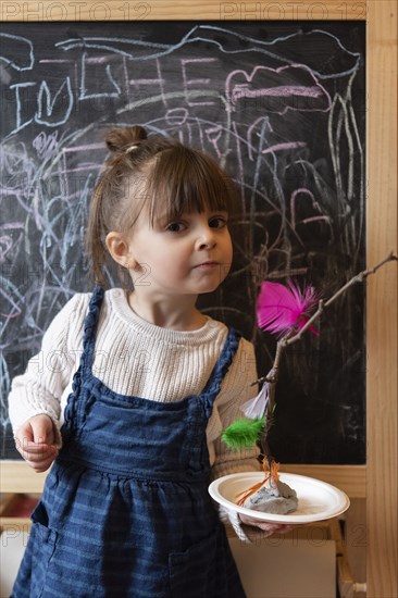 Girl holding stick and feather craft by blackboard