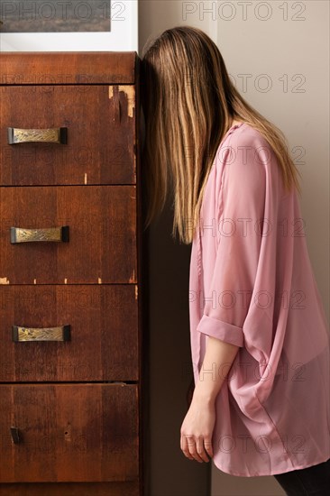 Young woman banging her head against wooden drawers