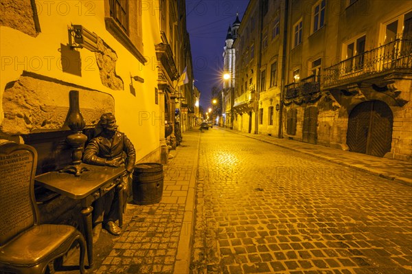 Sculpture of man sitting at table at night in Lviv, Ukraine