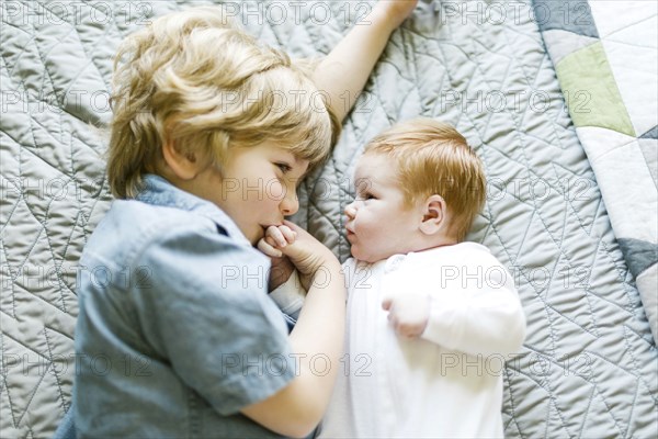 View directly above boy with his baby brother lying on bed