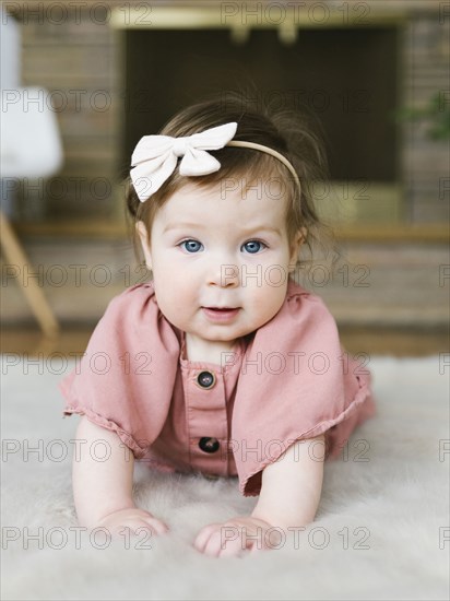 Baby girl wearing bow hair band lying on rug