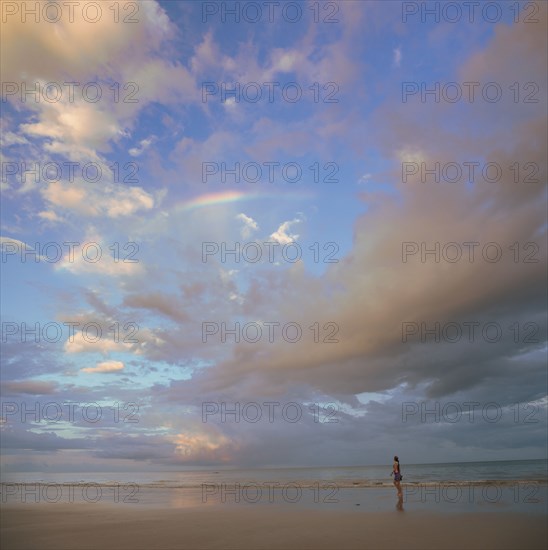 Cloudscape over woman walking on beach in Port Douglas, Australia