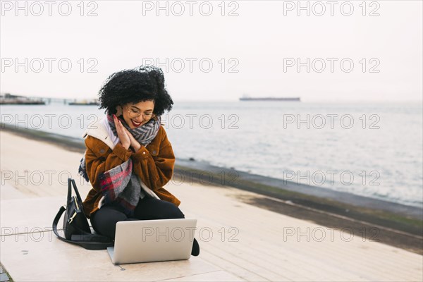 Young woman using laptop on waterfront in Lisbon, Portugal