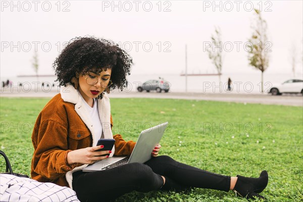 Young woman using laptop and smart phone in park