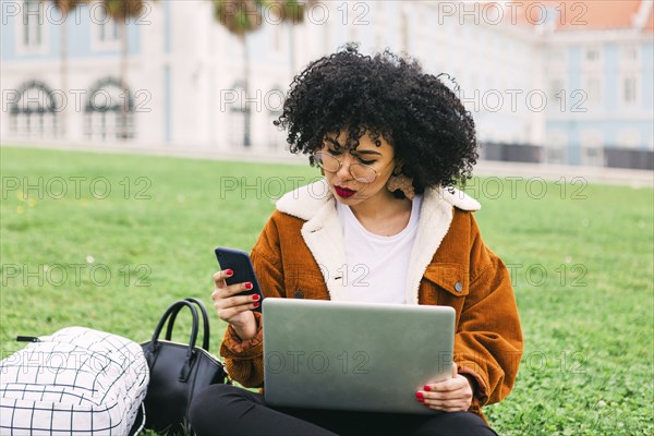 Young woman using laptop and smart phone in park