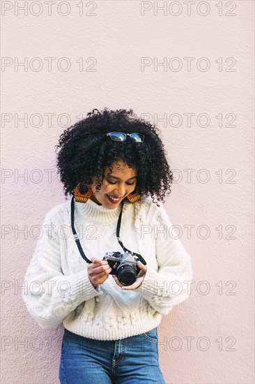 Young woman holding camera against pink wall