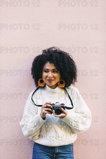 Young woman holding camera against pink wall