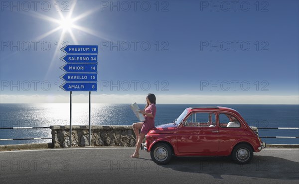 Woman holding map leaning on pink car