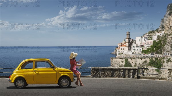Woman holding map leaning on yellow car in Atrani, Italy