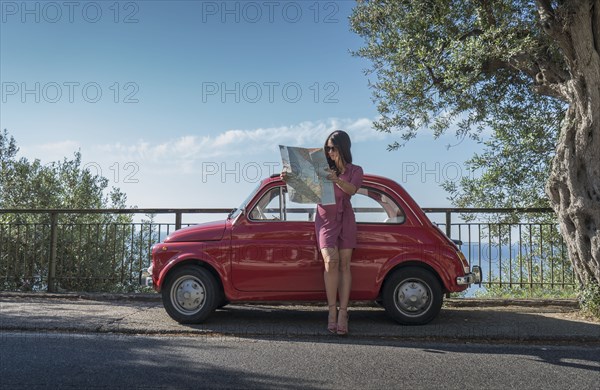 Woman holding map leaning on pink car
