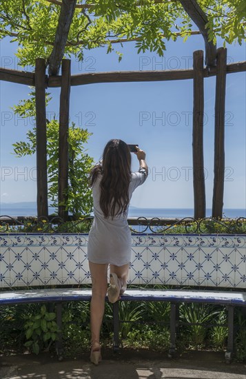 Woman taking photograph with smart phone under pergola