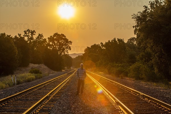Senior man standing between railroad tracks at sunset