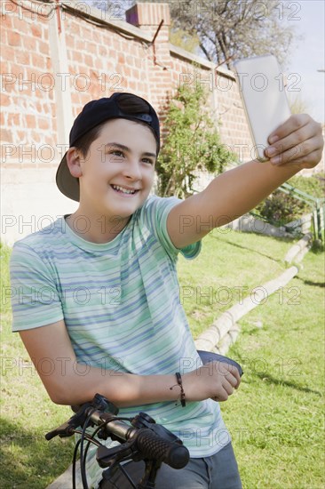 Teenage boy taking selfie while leaning on bicycle