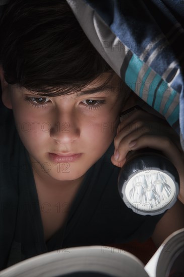 Boy reading with torch under blanket