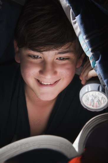 Boy reading with torch under blanket