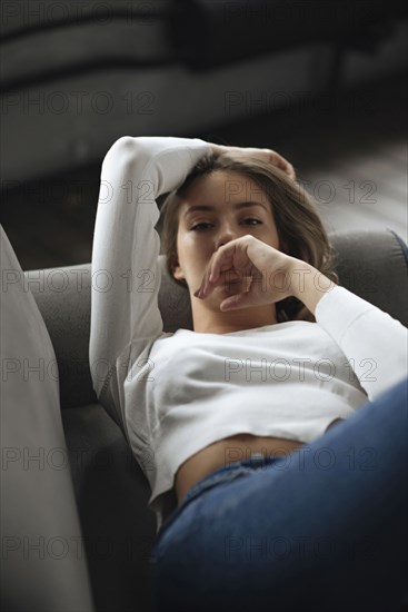 Young woman wearing white sweater lying on sofa