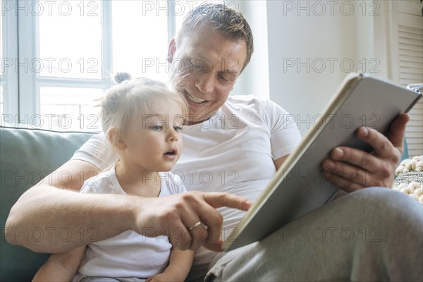 Father reading book to daughter on sofa