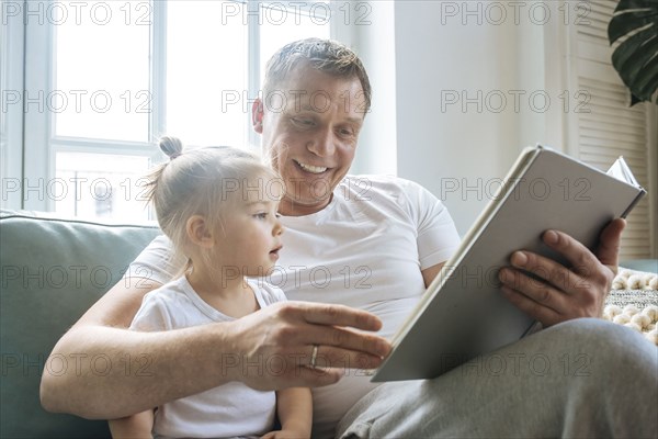 Father reading book to daughter on sofa