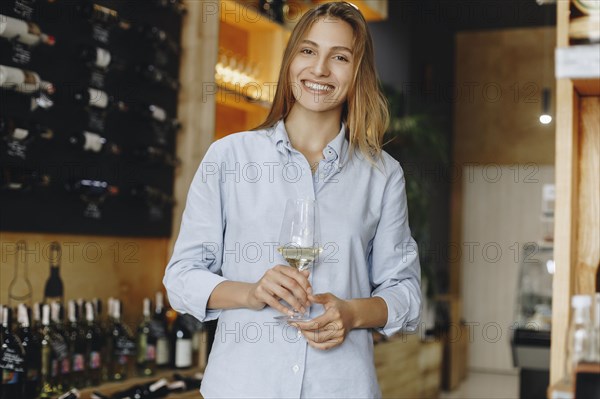 Smiling young woman holding glass of white wine