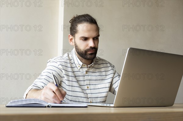 Young businessman with laptop writing in note pad