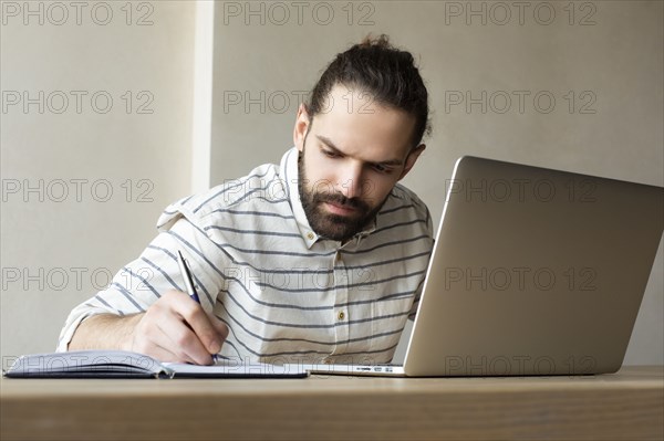 Young businessman with laptop writing in note pad