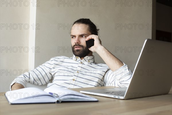 Young businessman on phone by laptop