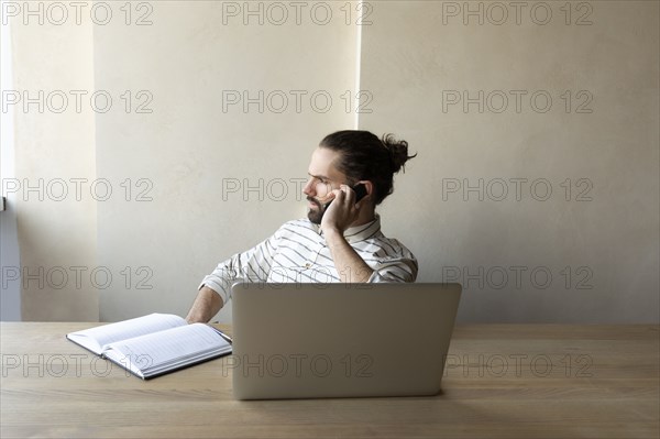 Young businessman on phone by laptop