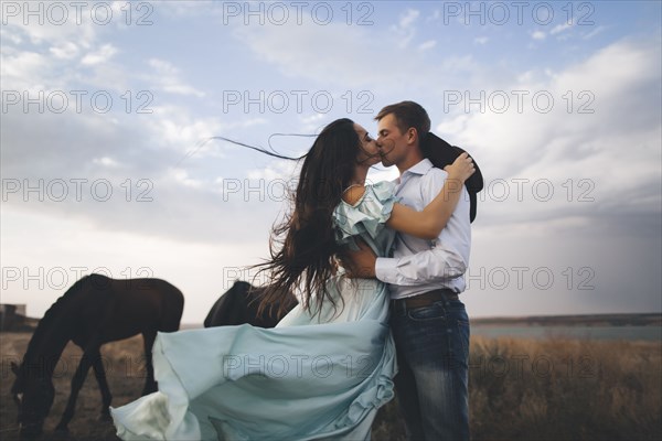 Young couple kissing in field by horses