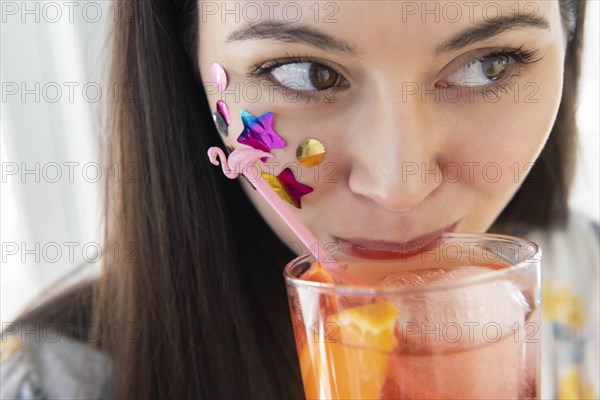 Woman with confetti on cheek drinking cocktail