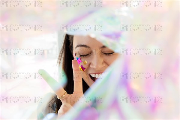 Woman with confetti on cheek making peace gesture