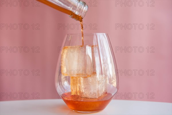 Liquor being poured into glass with ice cubes