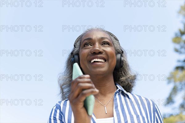 Smiling mature woman walking with headphones and smartphone