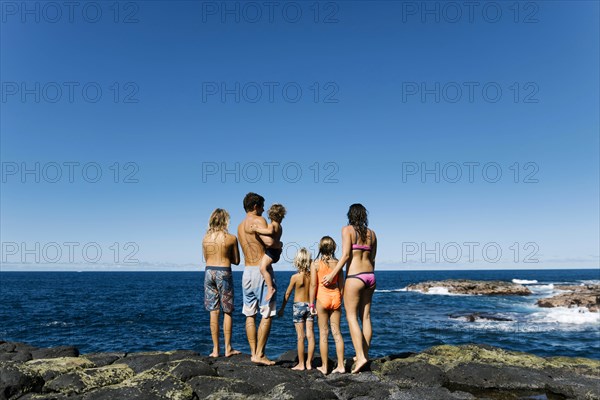 Rear view of family standing on rocks by sea