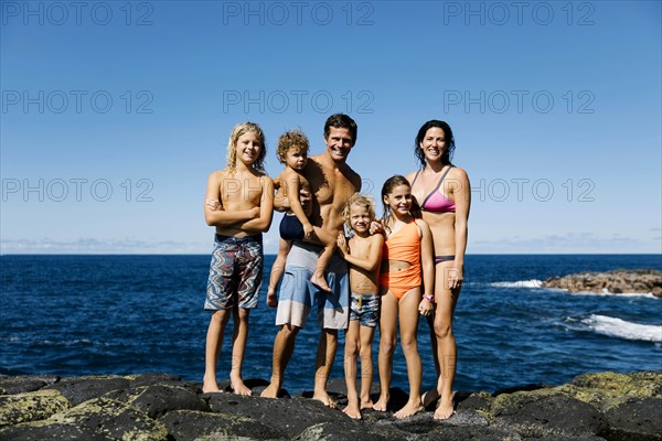 Smiling family standing on rocks by sea