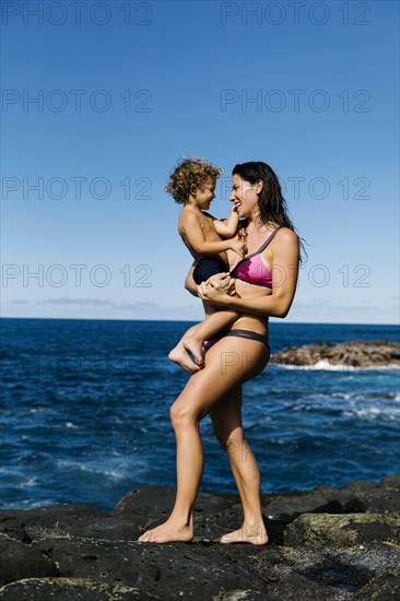 Mother carrying her son on rocks by sea
