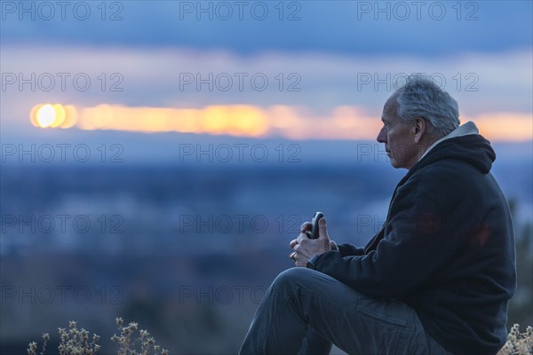 Seated man holding smart phone at sunset