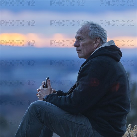 Seated man holding smart phone at sunset