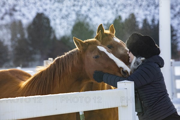 Woman wearing fur hat stroking horses