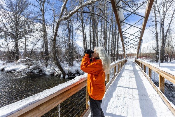 Mature woman using binoculars on snow covered footbridge