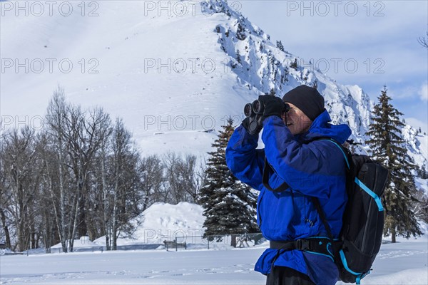 Senior man using binoculars by snow covered mountain in Sun Valley, Idaho, USA