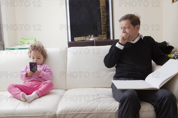 Girl using smart phone as her father reads book
