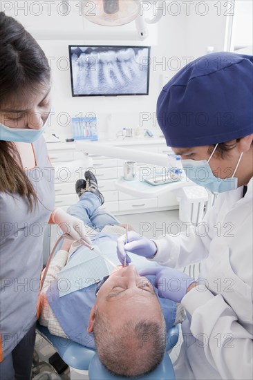 Dentist and hygienist cleaning patient's teeth