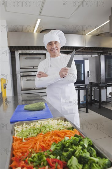 Smiling chef holding kitchen knife by raw vegetables