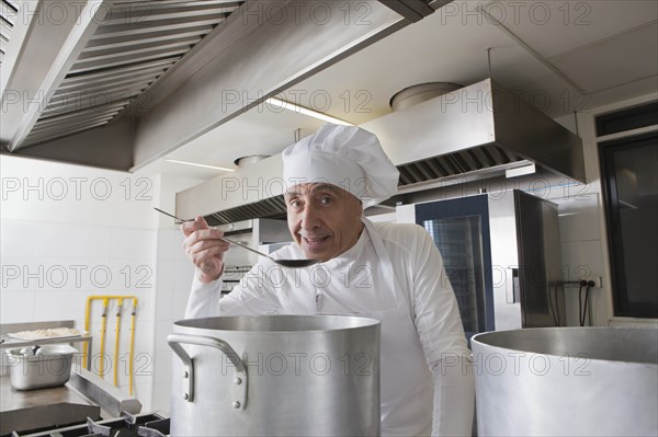 Smiling chef tasting food from pot