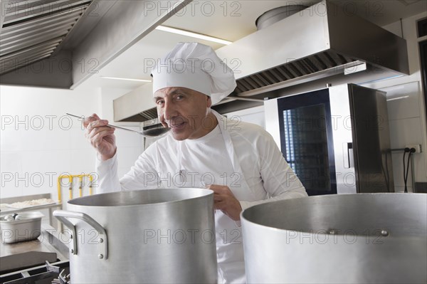 Smiling chef tasting food from pot