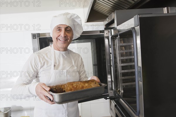 Chef holding meat in roasting tray by oven