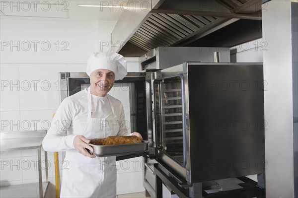 Chef holding meat in roasting tray by oven